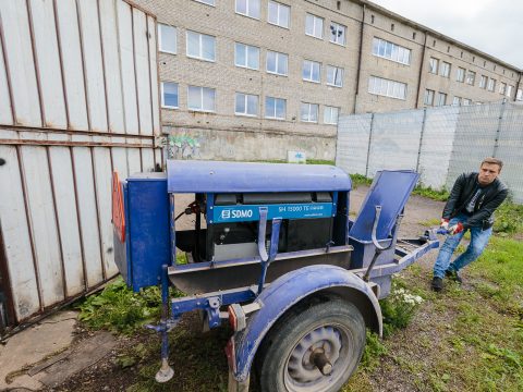 Электроснабжение автомастерской городские власти Нарвы отключили, и предприниматель Александр Брокк-младший вынужденно привлекает к работе дизельгенератор; электричество станет для него ощутимо дороже. Аналогично и с водоснабжением. На заднем плане изображено пустующее муниципальное здание и даже различима воздушная проводка к нему, которые обеспечивали электроснабжение автомастерской вплоть до 5 июля. На месте того здания должна быть построена к сентябрю 2022 года новая госгимназия. (Фото: Илья СМИРНОВ)
